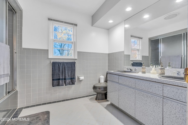 full bathroom featuring tile patterned flooring, shower / bath combination with glass door, vanity, toilet, and tile walls