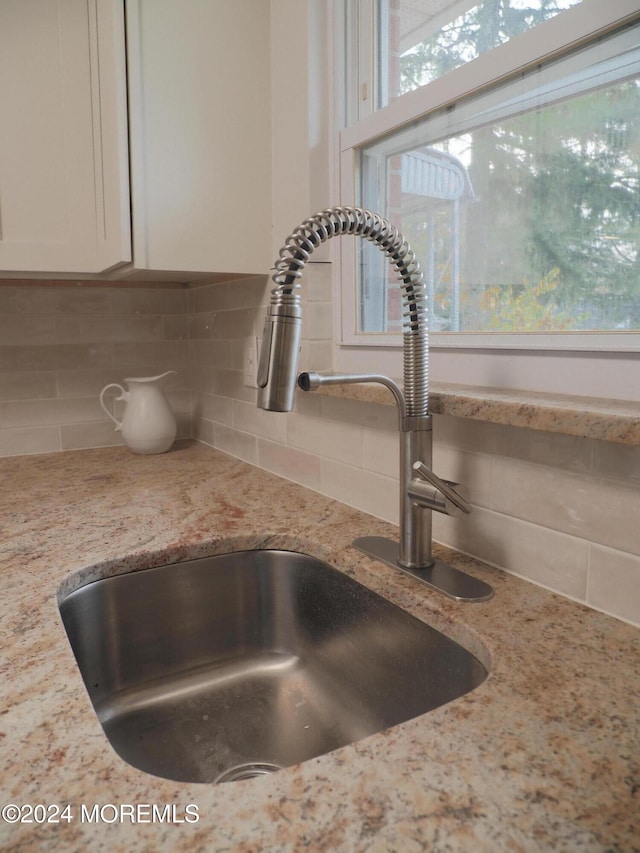 room details featuring white cabinetry, sink, tasteful backsplash, and light stone countertops