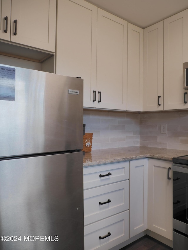 kitchen with light stone countertops, appliances with stainless steel finishes, backsplash, and white cabinets