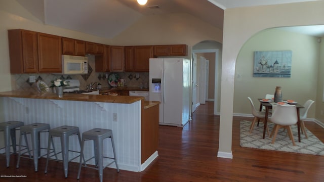 kitchen with backsplash, vaulted ceiling, kitchen peninsula, white appliances, and a breakfast bar area