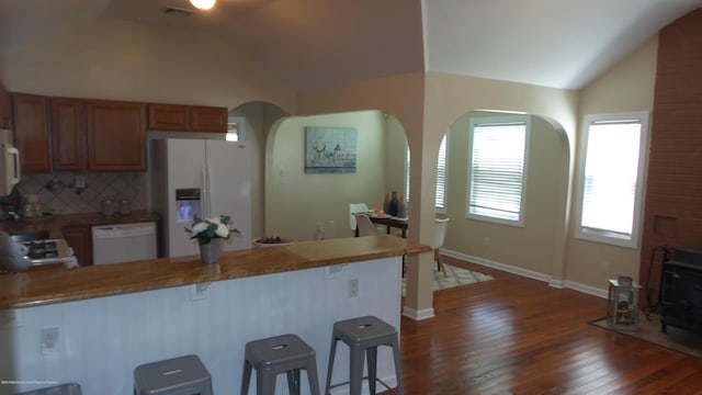 kitchen featuring tasteful backsplash, white appliances, dark hardwood / wood-style flooring, lofted ceiling, and a breakfast bar