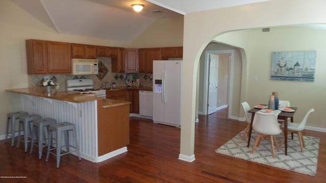 kitchen with white appliances, tasteful backsplash, kitchen peninsula, vaulted ceiling, and a breakfast bar area