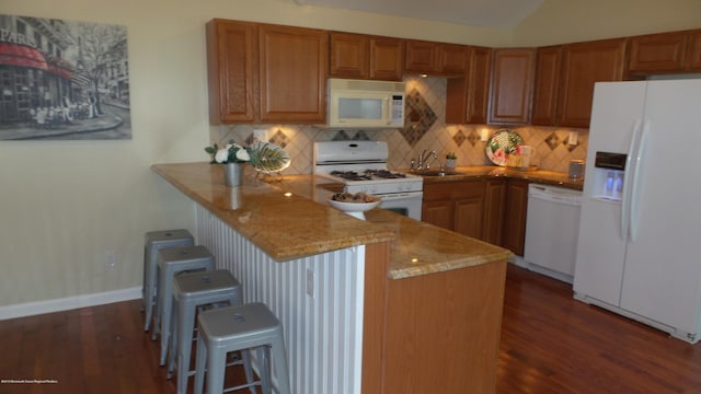 kitchen featuring a breakfast bar, kitchen peninsula, sink, white appliances, and dark wood-type flooring