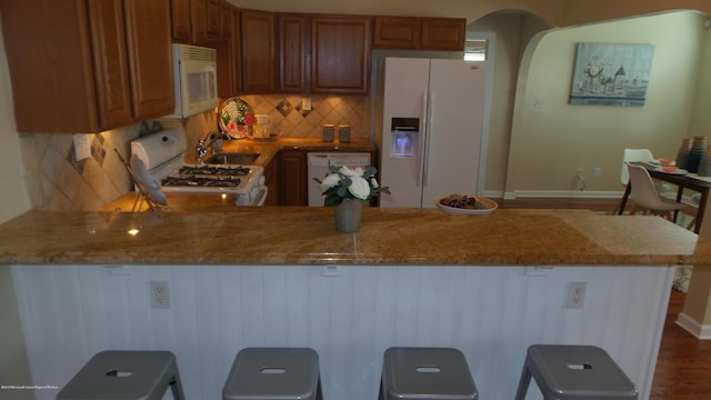 kitchen featuring light stone countertops, a breakfast bar area, decorative backsplash, and white appliances