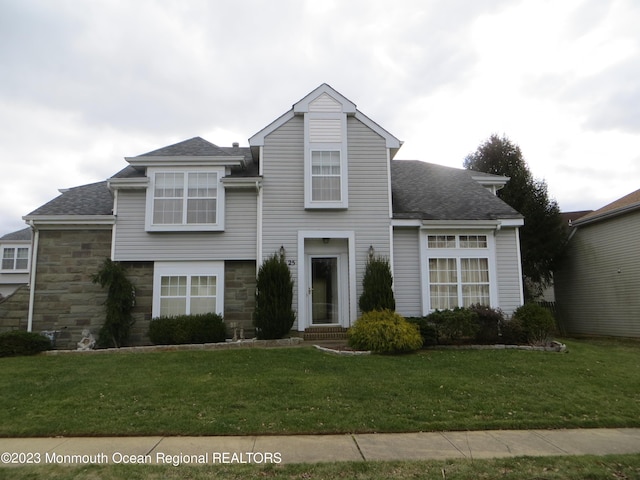 view of front of house featuring stone siding, roof with shingles, and a front yard