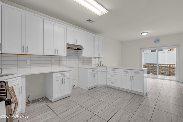 kitchen with kitchen peninsula, tasteful backsplash, sink, stainless steel range oven, and white cabinets