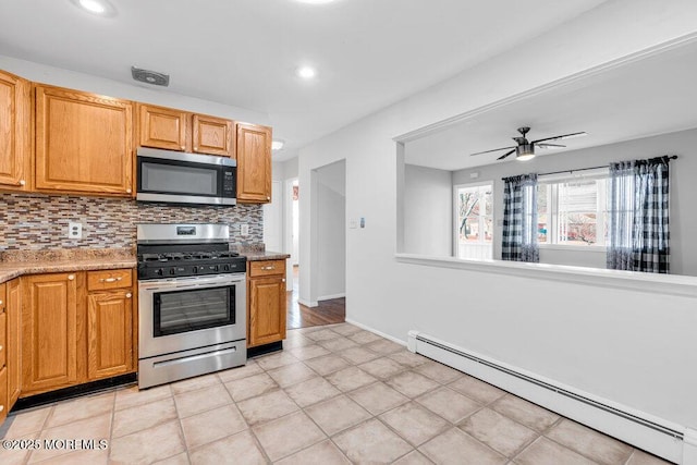 kitchen with a baseboard radiator, decorative backsplash, appliances with stainless steel finishes, a ceiling fan, and light stone countertops