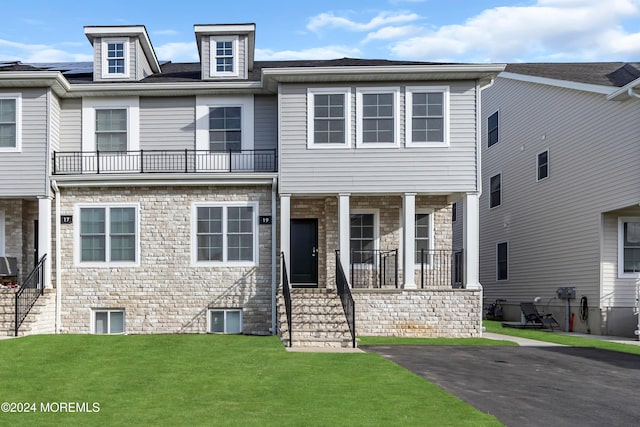 view of property featuring covered porch, a balcony, and a front lawn