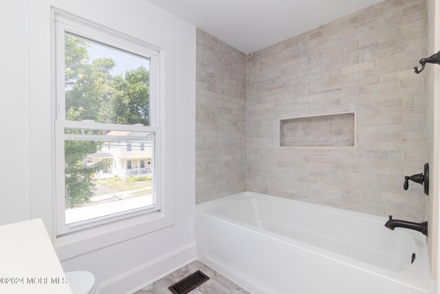 bathroom with tile patterned flooring, a healthy amount of sunlight, tiled shower / bath combo, and toilet