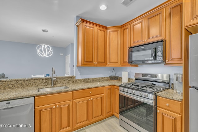 kitchen with light stone counters, sink, stainless steel appliances, and light hardwood / wood-style flooring