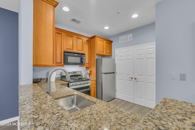 kitchen featuring light stone counters, sink, stainless steel appliances, and light hardwood / wood-style floors