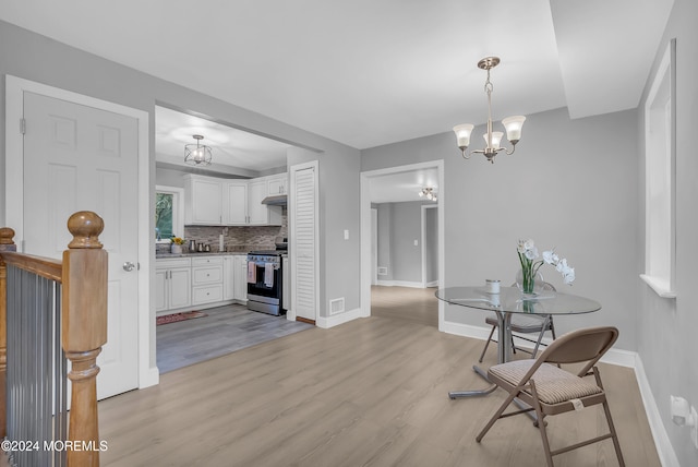 interior space with decorative backsplash, light wood-type flooring, stainless steel range, white cabinets, and hanging light fixtures