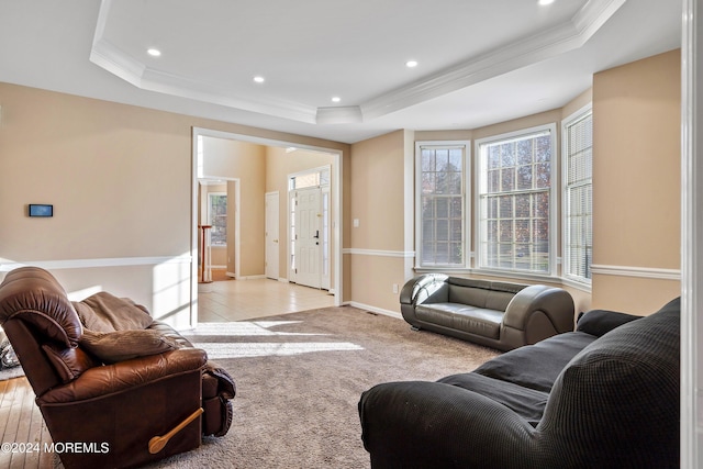 living room with light wood-type flooring, crown molding, and a tray ceiling