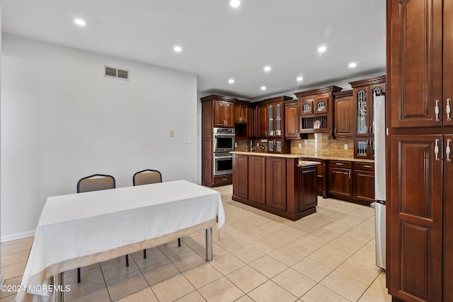 kitchen featuring stainless steel appliances, a kitchen island, decorative backsplash, dark brown cabinets, and light tile patterned flooring