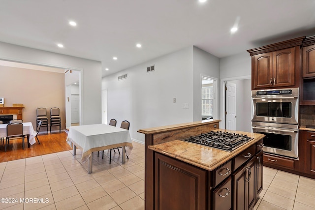 kitchen with a center island, light tile patterned flooring, stainless steel appliances, and dark brown cabinets