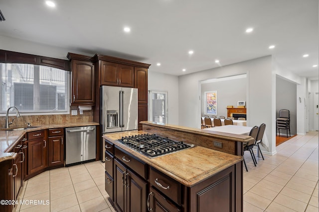 kitchen with a center island, sink, light tile patterned floors, appliances with stainless steel finishes, and dark brown cabinetry