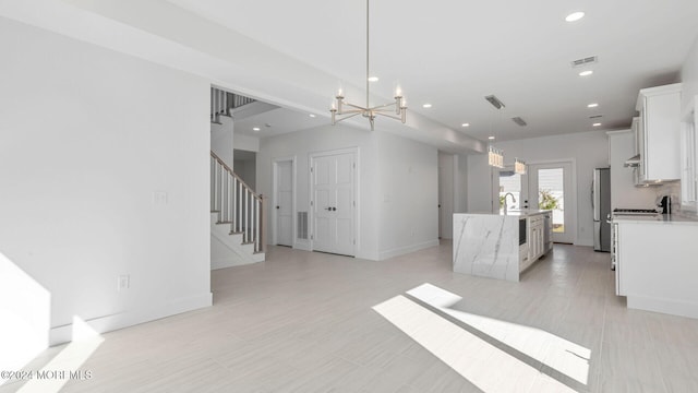 kitchen with a kitchen island with sink, an inviting chandelier, white cabinets, stainless steel fridge, and decorative light fixtures