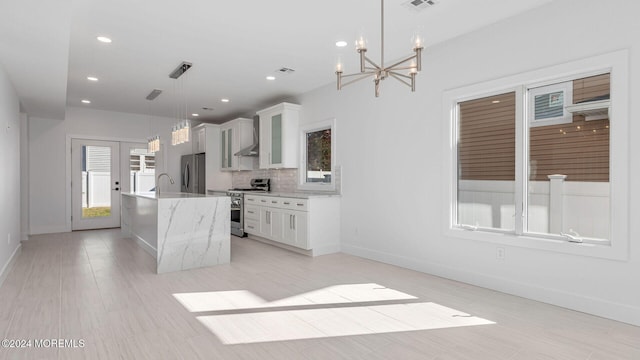 kitchen with backsplash, a kitchen island with sink, appliances with stainless steel finishes, decorative light fixtures, and white cabinetry