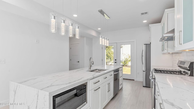 kitchen with white cabinets, appliances with stainless steel finishes, a center island with sink, and sink