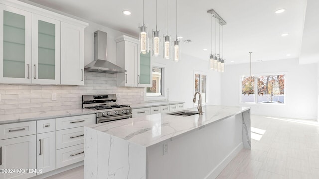 kitchen with a kitchen island with sink, white cabinets, stainless steel range with gas cooktop, hanging light fixtures, and wall chimney exhaust hood