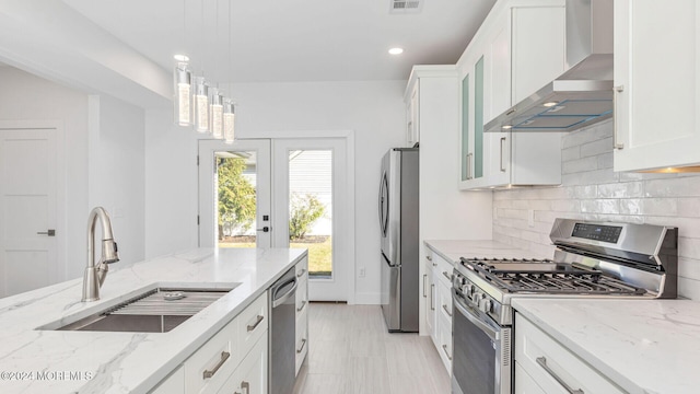 kitchen with sink, wall chimney exhaust hood, decorative light fixtures, white cabinets, and appliances with stainless steel finishes