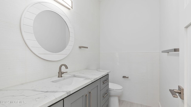 bathroom with vanity, toilet, and tile walls