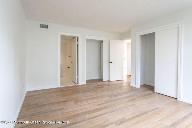 unfurnished bedroom featuring light hardwood / wood-style floors, a textured ceiling, and ensuite bath