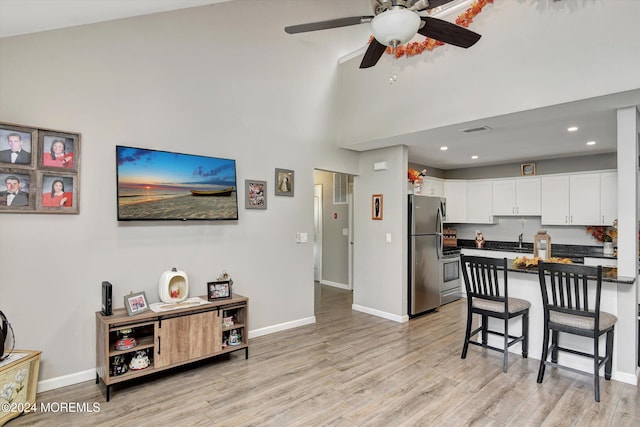 kitchen featuring high vaulted ceiling, white cabinets, light hardwood / wood-style flooring, appliances with stainless steel finishes, and a breakfast bar area