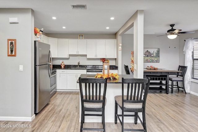 kitchen featuring white cabinets, a breakfast bar area, ceiling fan, light hardwood / wood-style floors, and stainless steel appliances