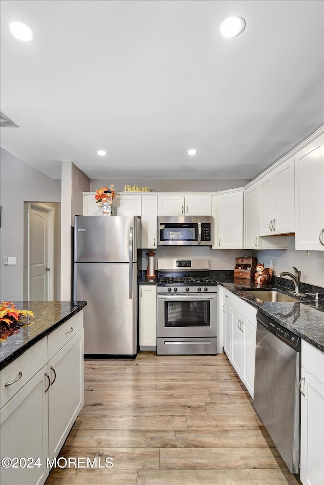 kitchen with dark stone counters, stainless steel appliances, white cabinetry, and light hardwood / wood-style floors