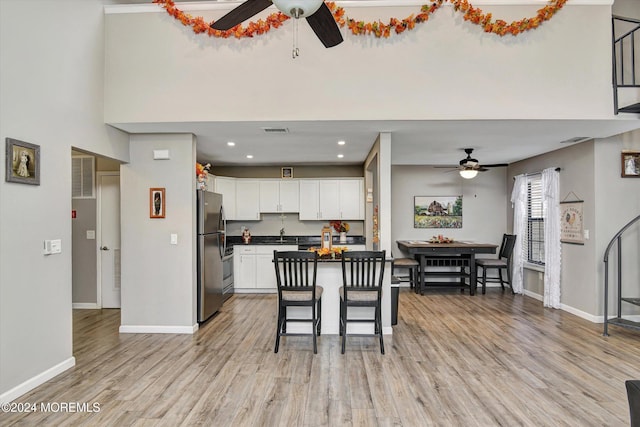 kitchen featuring white cabinetry, a breakfast bar area, stainless steel refrigerator, and light hardwood / wood-style flooring