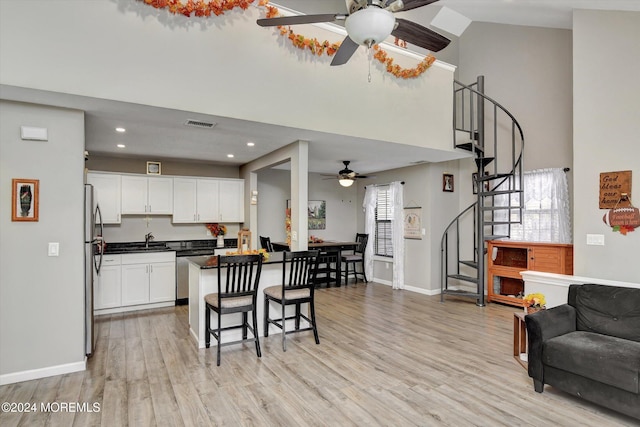 kitchen with appliances with stainless steel finishes, a kitchen breakfast bar, ceiling fan, light hardwood / wood-style flooring, and white cabinets