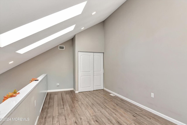 bonus room with vaulted ceiling with skylight and light wood-type flooring