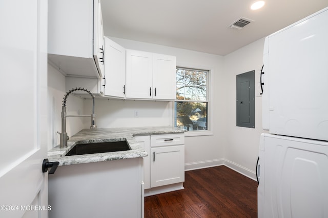 kitchen featuring electric panel, sink, dark hardwood / wood-style floors, stacked washer / drying machine, and white cabinetry