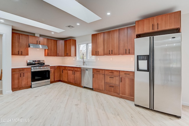 kitchen featuring appliances with stainless steel finishes, a skylight, light hardwood / wood-style floors, and sink