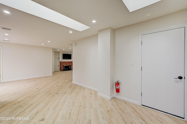 interior space with a skylight, light hardwood / wood-style flooring, and a brick fireplace