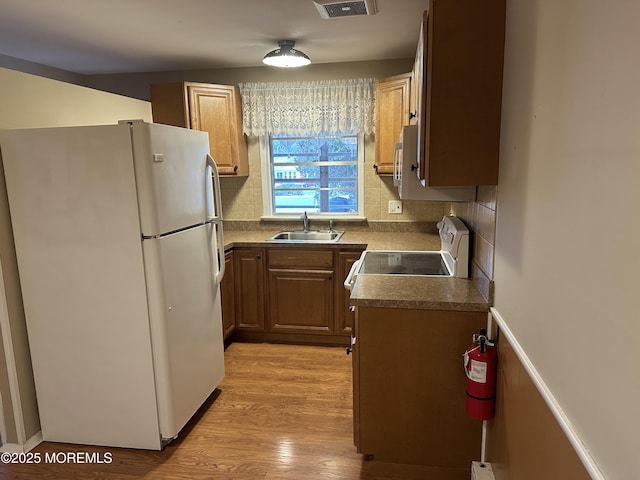 kitchen featuring sink, white appliances, light hardwood / wood-style floors, and backsplash