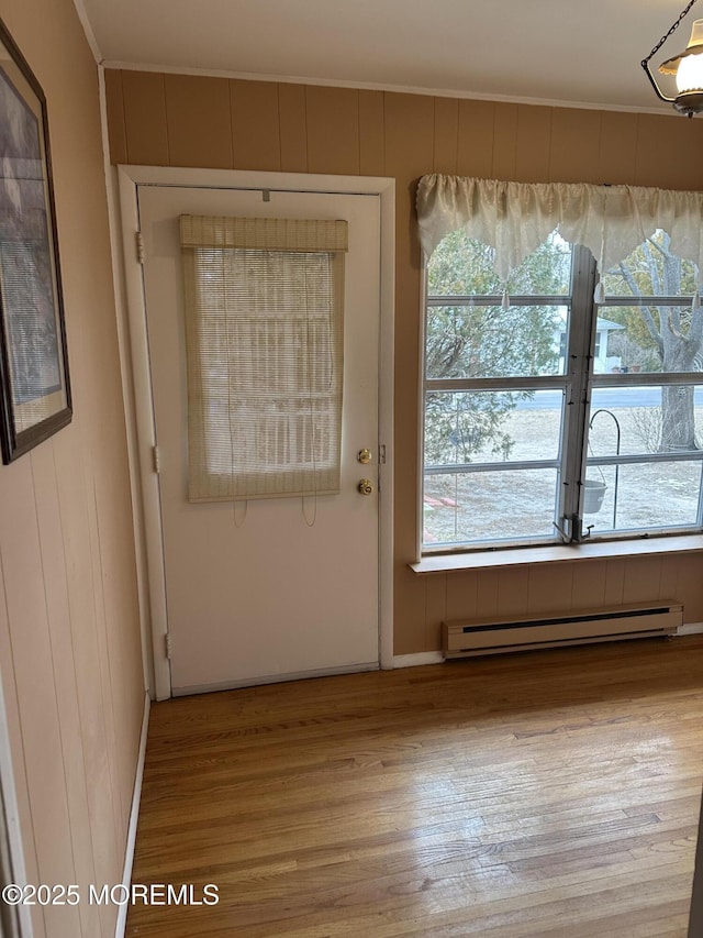 doorway featuring light wood-type flooring, crown molding, a baseboard heating unit, and wood walls