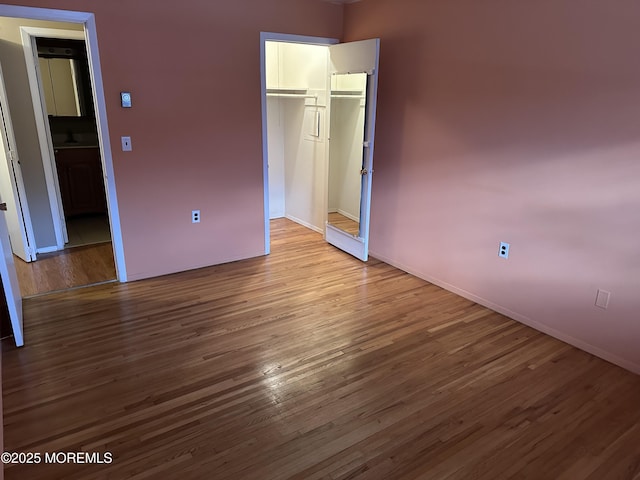 unfurnished bedroom with wood-type flooring, a walk in closet, and a closet