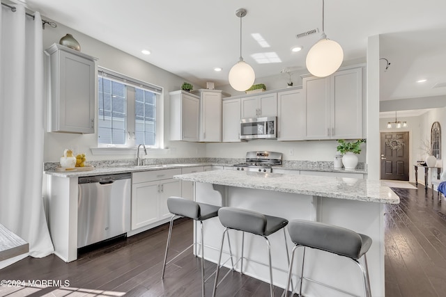 kitchen featuring visible vents, appliances with stainless steel finishes, a breakfast bar, dark wood-style flooring, and a sink