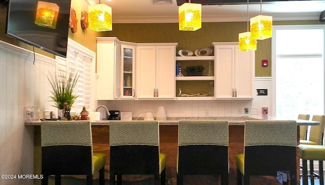 kitchen with ornamental molding, hanging light fixtures, a kitchen bar, white cabinetry, and open shelves