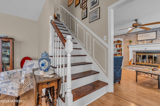 stairs featuring ceiling fan, built in features, brick wall, hardwood / wood-style floors, and a fireplace