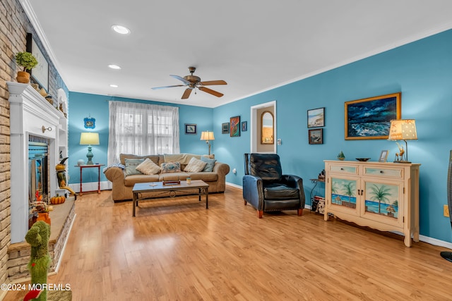 living room featuring a brick fireplace, crown molding, ceiling fan, and light wood-type flooring