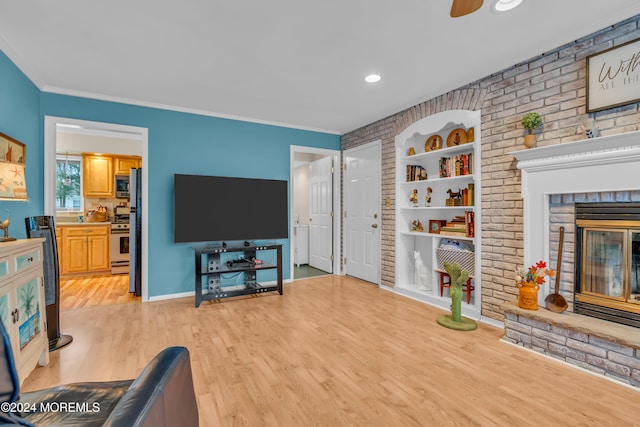 living room with crown molding, a brick fireplace, ceiling fan, light wood-type flooring, and brick wall