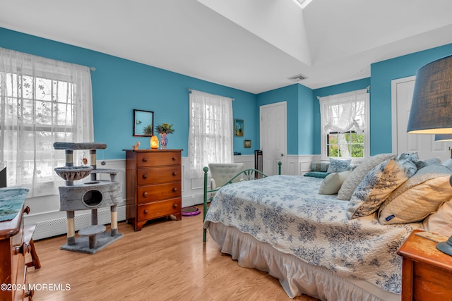 bedroom featuring a baseboard radiator, light hardwood / wood-style floors, and vaulted ceiling