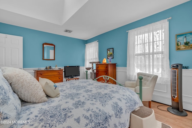 bedroom with multiple windows, wood-type flooring, and a baseboard heating unit