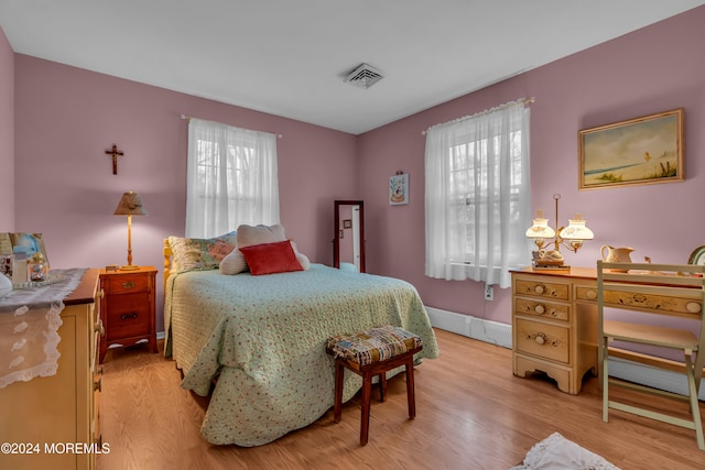 bedroom with light hardwood / wood-style flooring, a baseboard radiator, and multiple windows