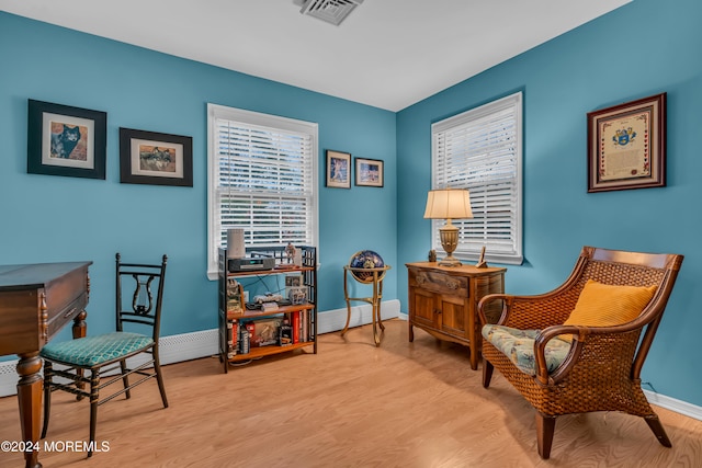 living area with light hardwood / wood-style floors, baseboard heating, and a wealth of natural light