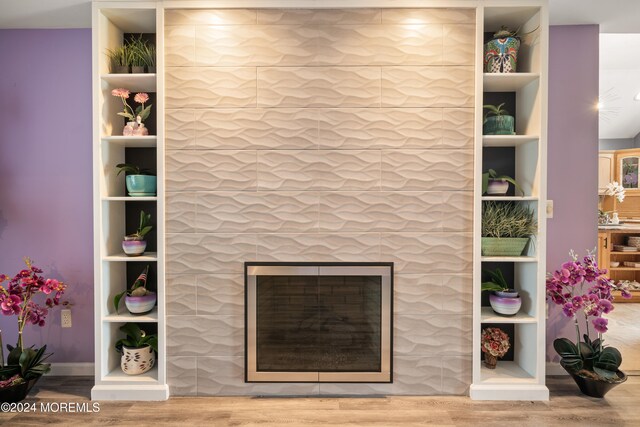 room details with wood-type flooring, built in features, and a tiled fireplace