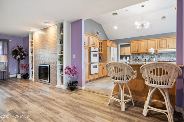 kitchen featuring white appliances, light hardwood / wood-style flooring, kitchen peninsula, a breakfast bar area, and a chandelier